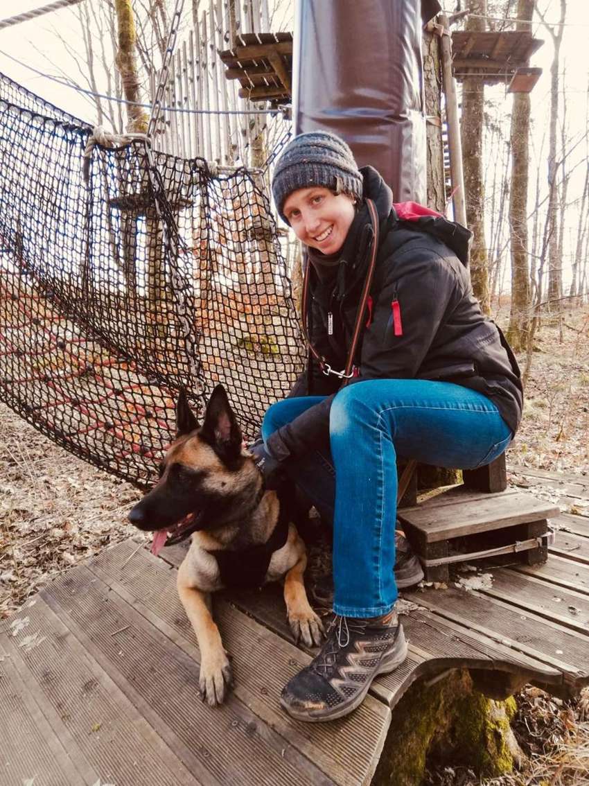 Janina sitzt mit ihrem Malinois auf einem Holzsteg